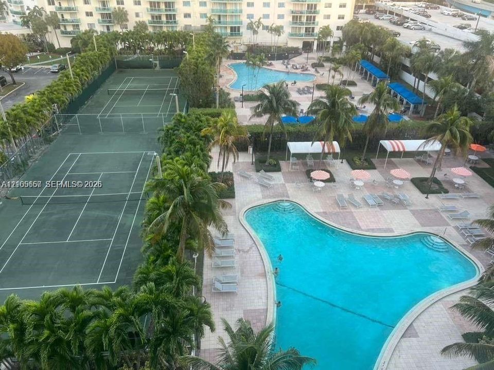 Community amenities featuring two tennis courts, multiple swimming pools, and paved sun decks with mature palm trees