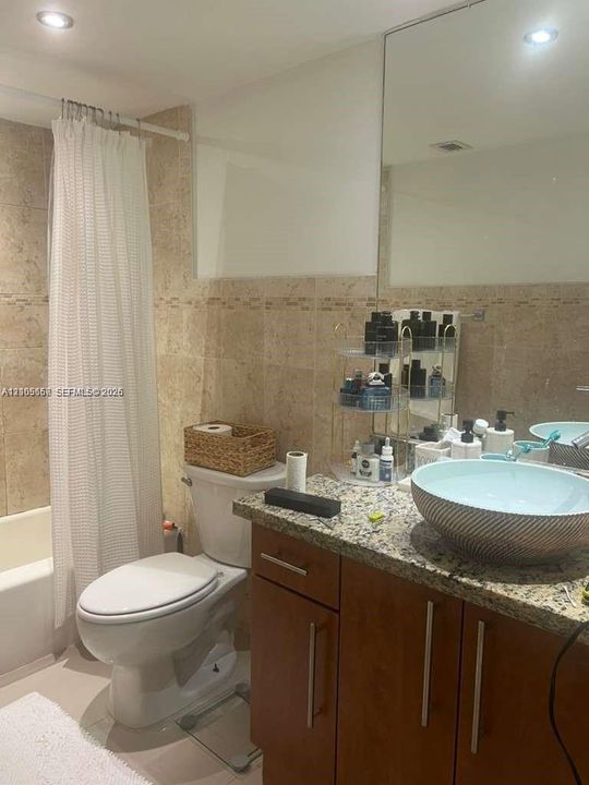 Bathroom featuring natural stone wall tile, vessel sink, stone-surface countertop, wood-finish cabinetry, and recessed lighting