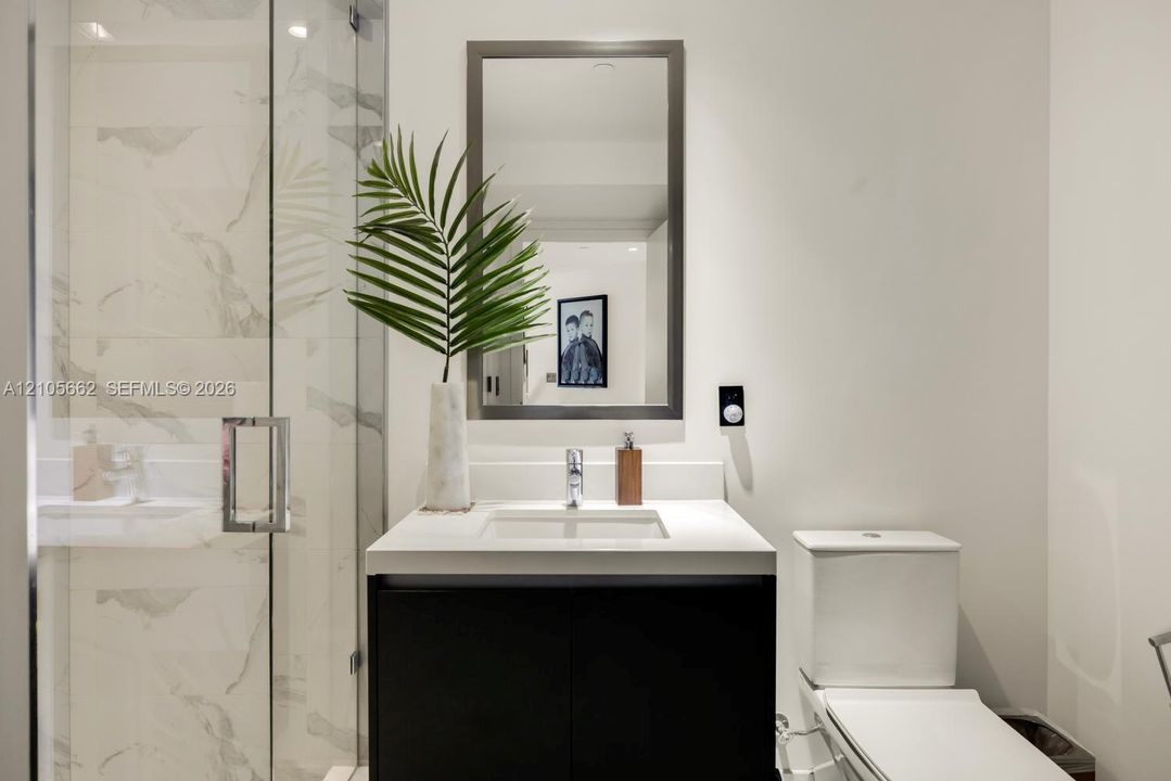 Modern vanity with a countertop basin and cabinet storage, framed wall mirror, glass-enclosed shower with large-format tile surround, and dual-flush toilet