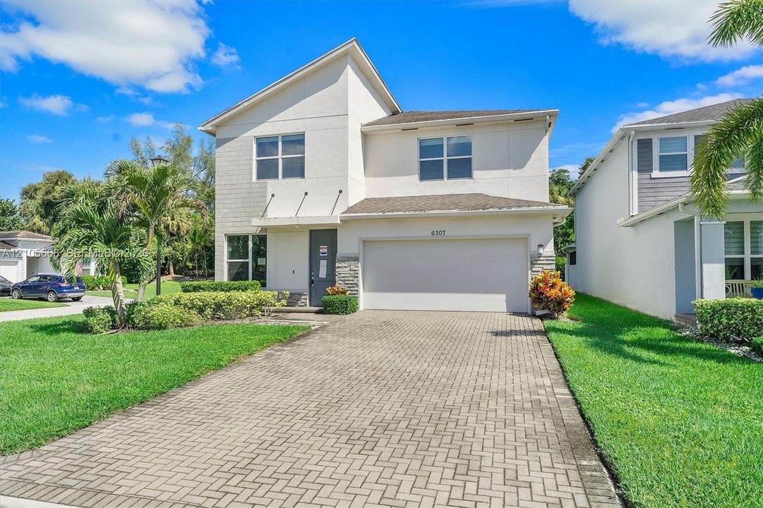 Two-story exterior featuring a light-toned stucco façade, stone veneer accents, a multi-paneled garage door, and a herringbone-patterned paved driveway