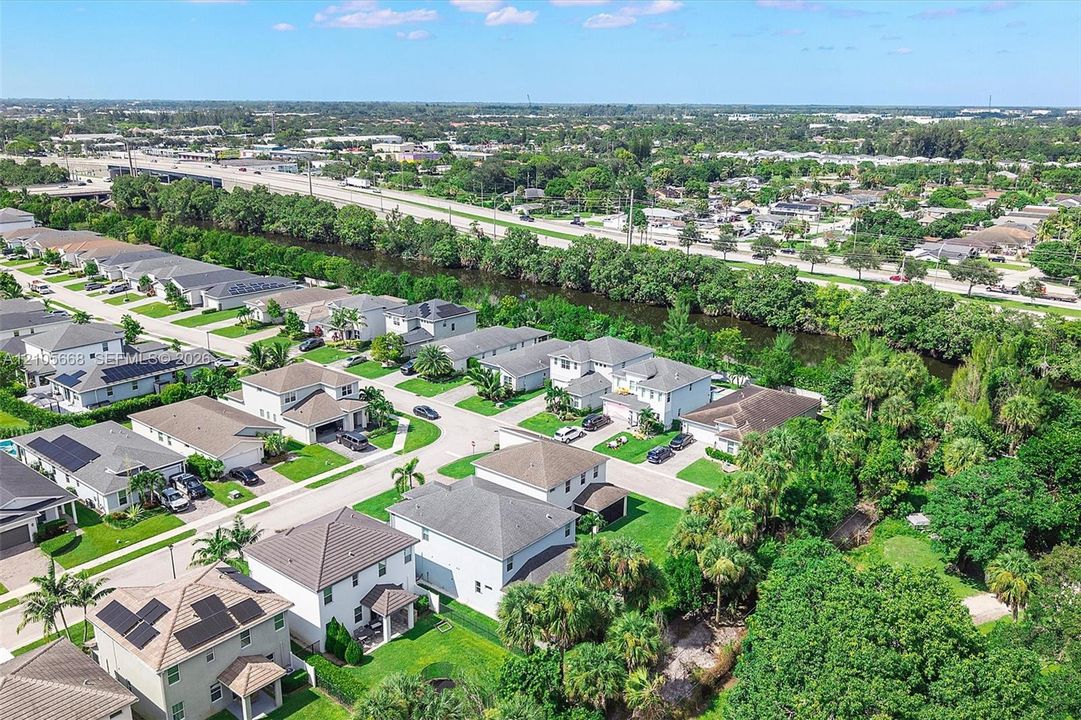 Aerial perspective of a suburban neighborhood featuring concrete tile roofing, solar panel arrays, manicured lawns, and perimeter landscaping