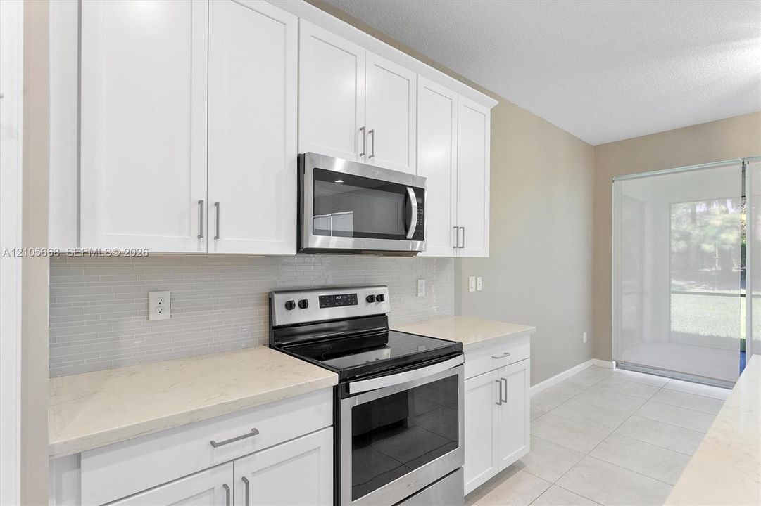 Kitchen featuring white cabinetry, stainless steel appliances, neutral countertops, linear tile backsplash, and ceramic tile flooring