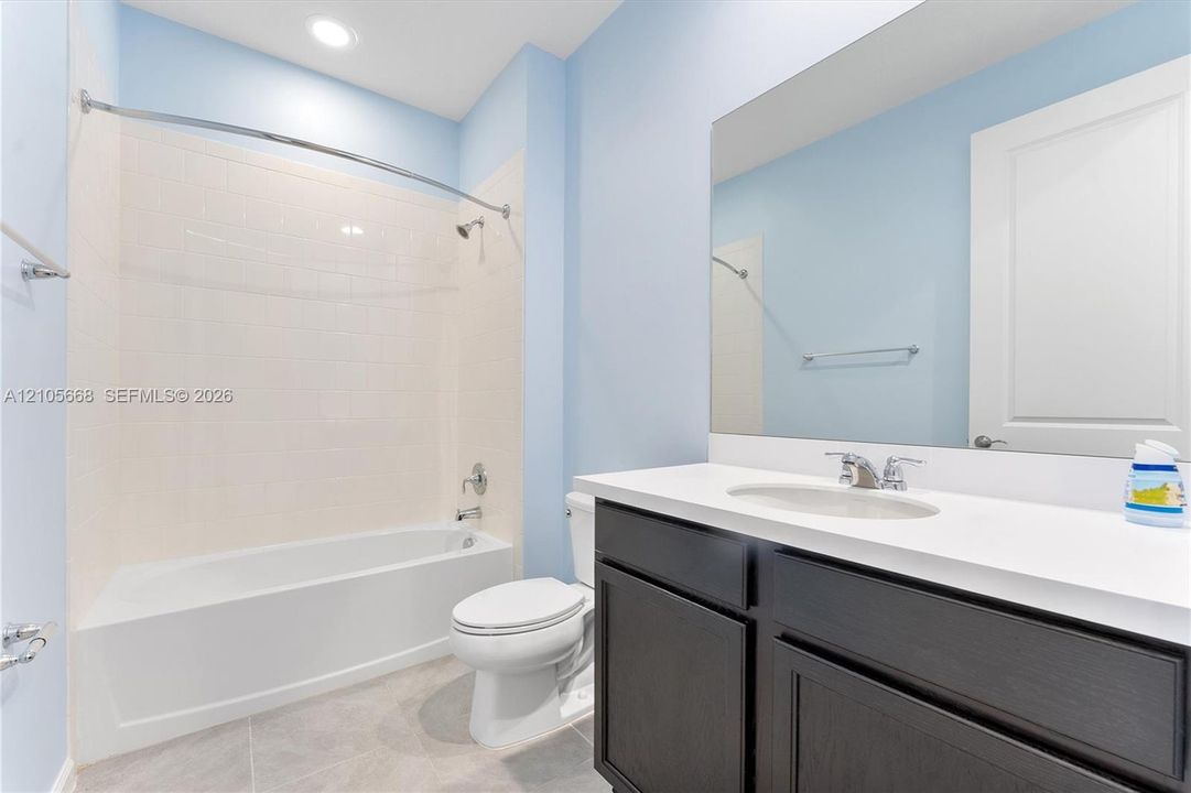 Bathroom featuring a vanity with a white countertop and rectangular sink, dark cabinetry, a full-width vanity mirror, a bathtub-shower combination with tiled surround, and tile flooring