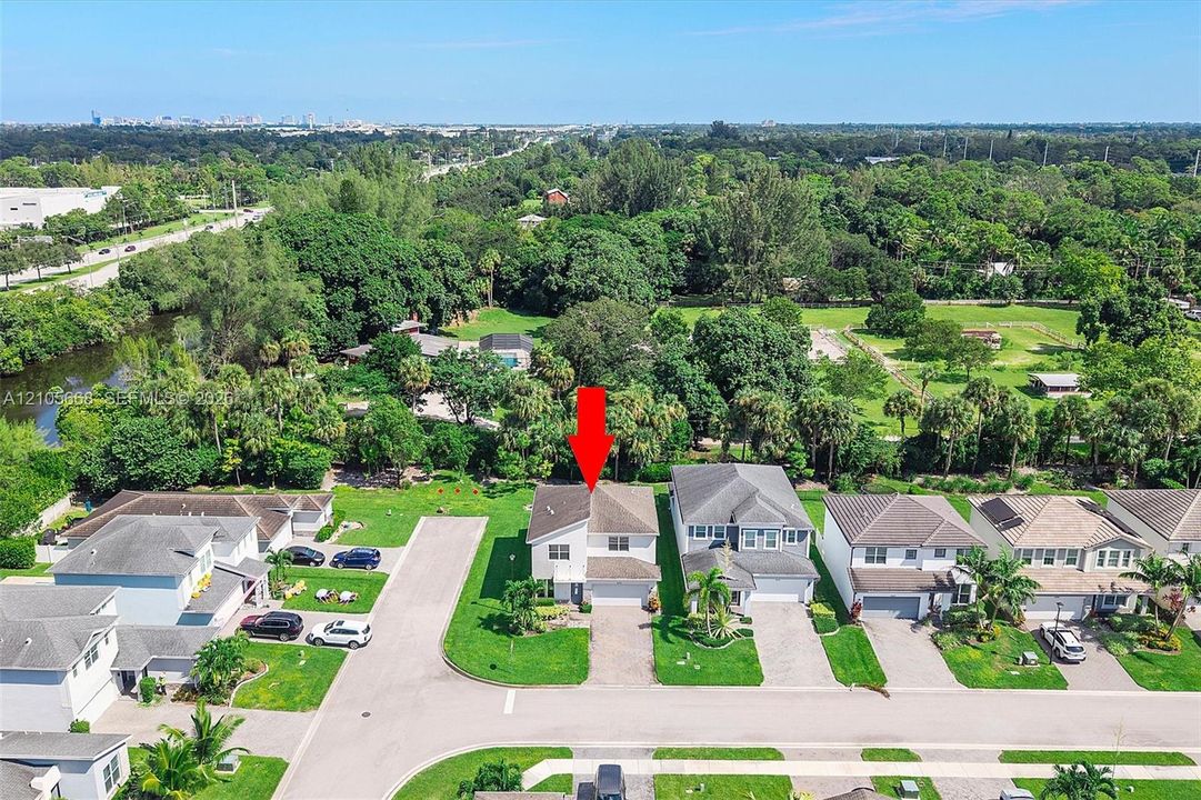 Aerial view of a residential property featuring a multi-story home with an attached garage, manicured landscaping with mature trees, and a circular driveway