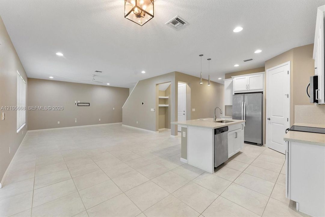 Open-concept space featuring ceramic tile flooring, recessed lighting, kitchen island with integrated stainless steel sink, white shaker-style cabinetry, and stainless steel appliances