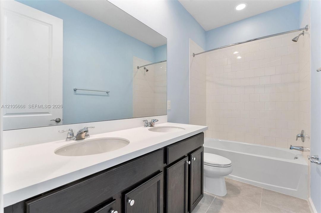 Bathroom featuring a double-sink vanity with a solid-surface countertop, full-width vanity mirror, tile flooring, and a bathtub-shower combination with tile surround