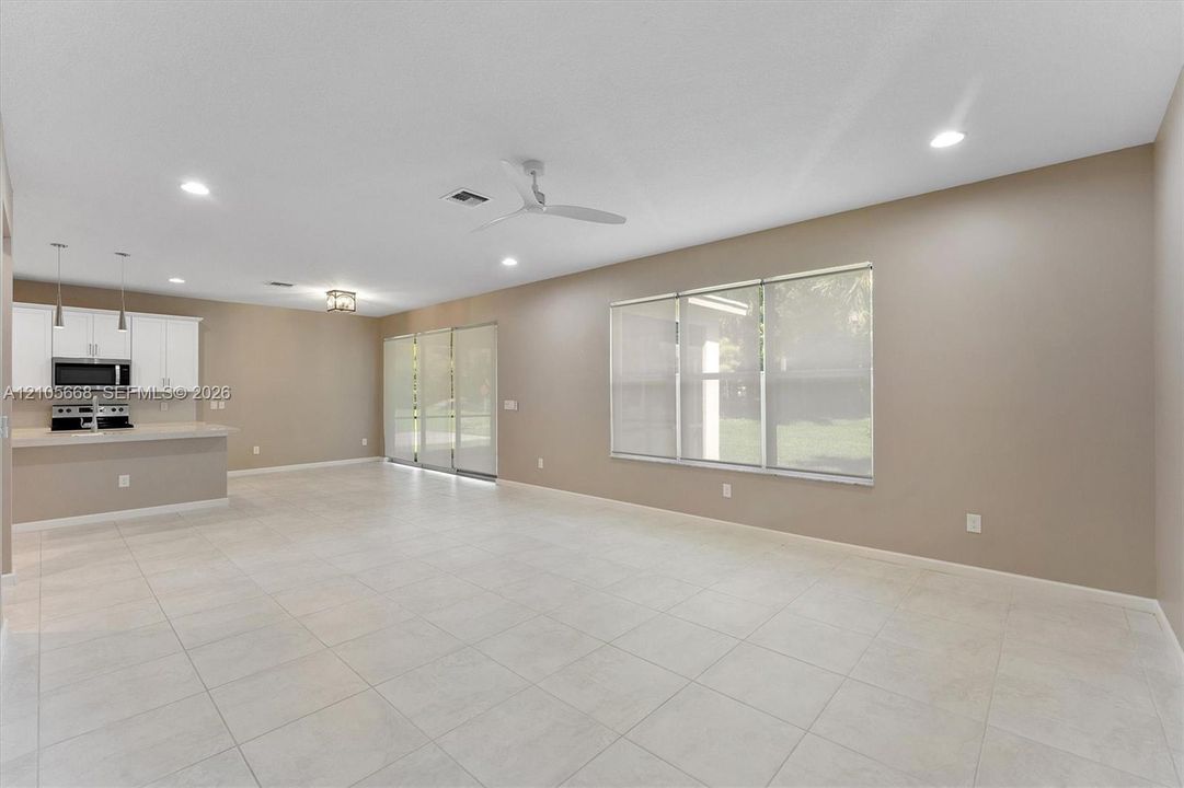 Open-concept interior featuring neutral wall tones, large-format tile flooring, recessed lighting, white cabinetry with built-in microwave, and oversized windows
