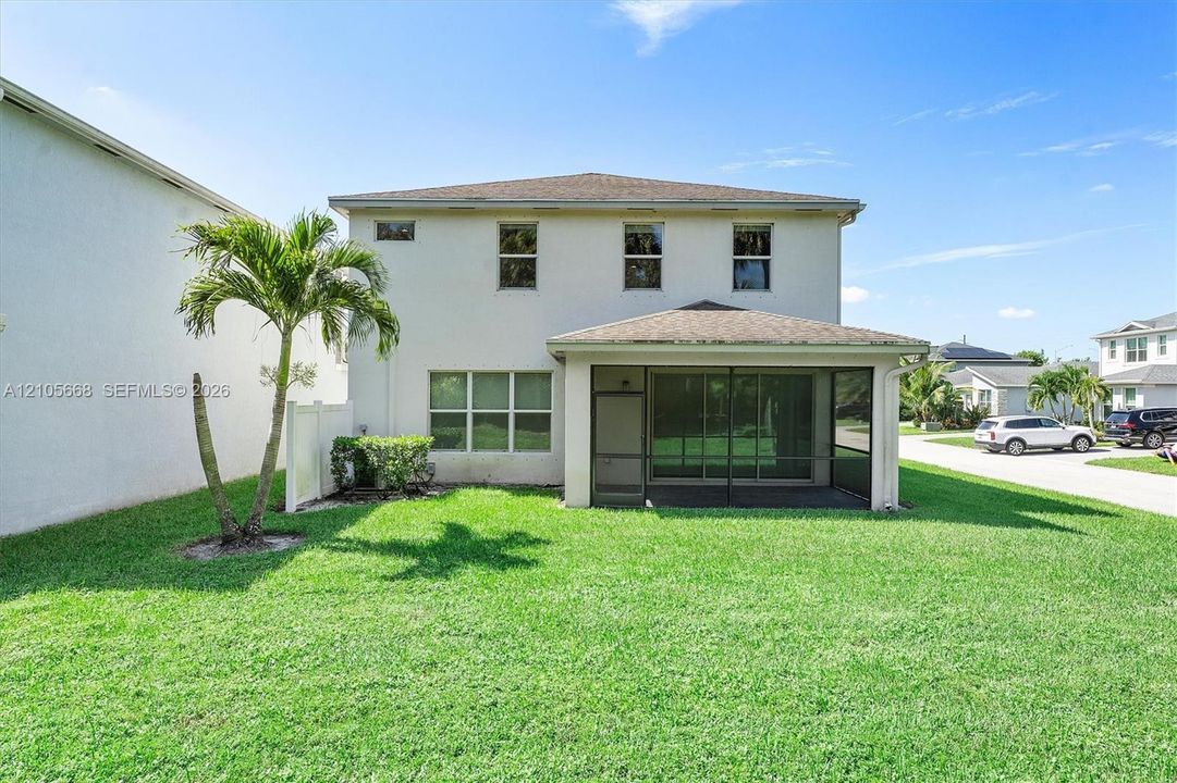 Two-story exterior featuring a stucco facade, a hip roof, a covered screened-in lanai, and a sodded lawn with palm tree landscaping