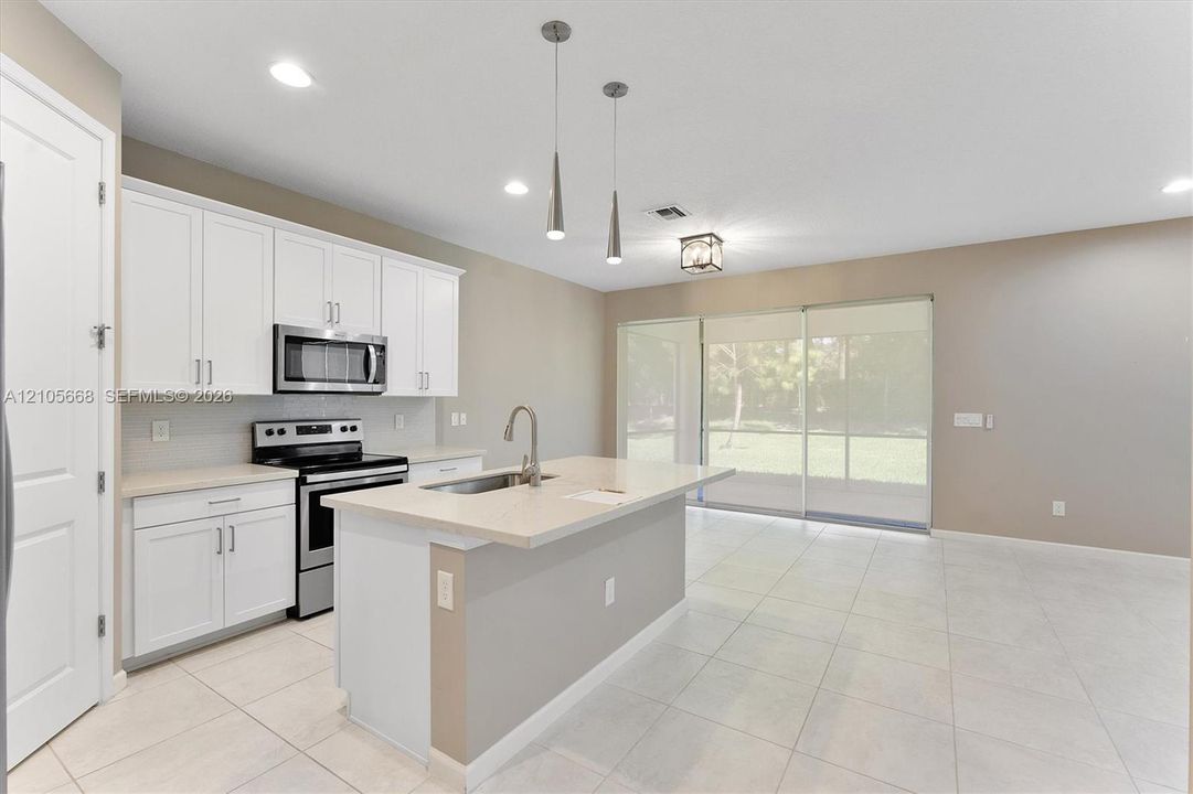Kitchen featuring white shaker-style cabinetry, a central island with a solid-surface countertop, stainless steel appliances, dual pendant lighting, and neutral tile flooring