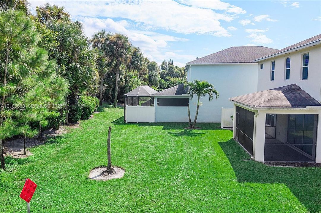 Backyard featuring a screened-in lanai, manicured lawn, established palm trees, and perimeter landscaping