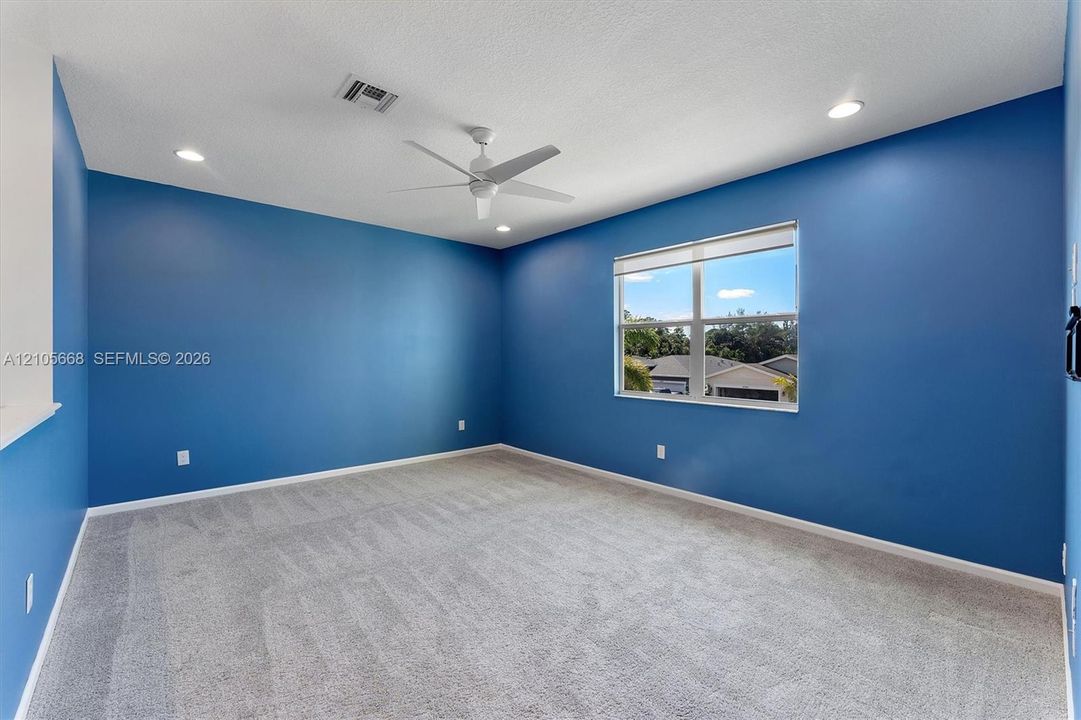 Neutral-toned carpeting, recessed lighting, ceiling fan, and large window with blinds