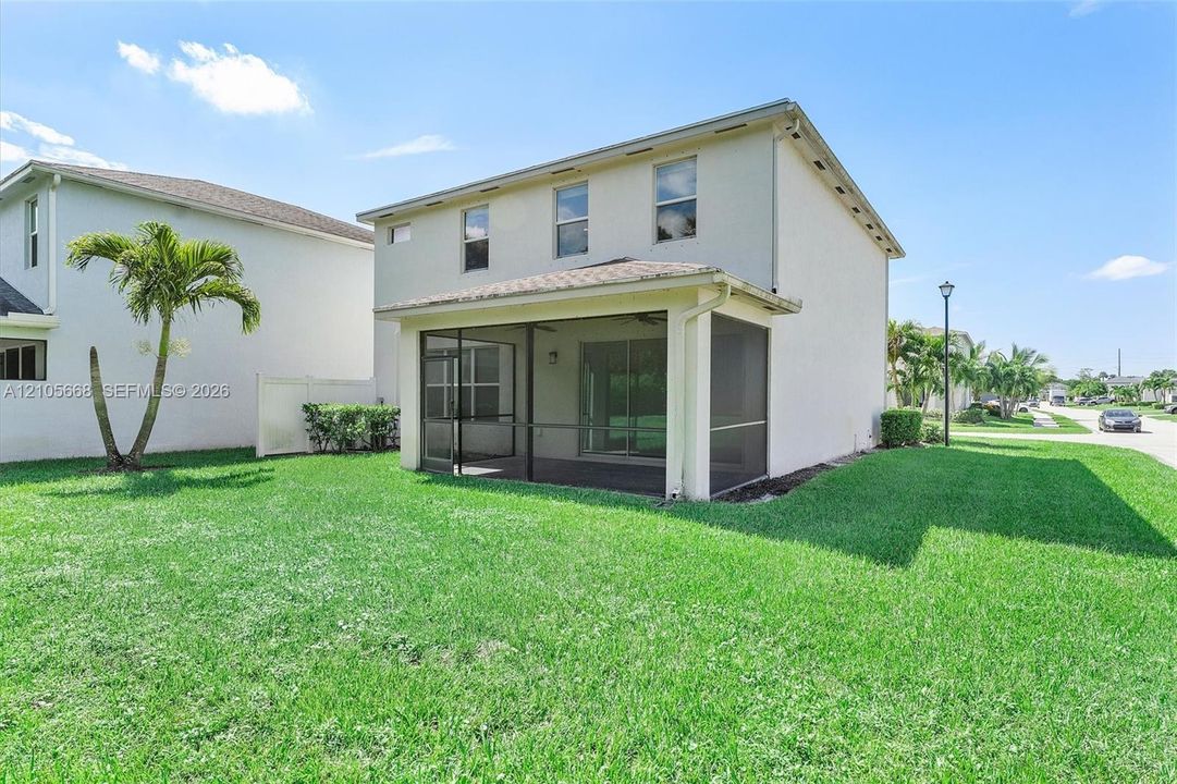 Two-story exterior featuring a stucco facade, screened-in rear lanai, and expansive lawn