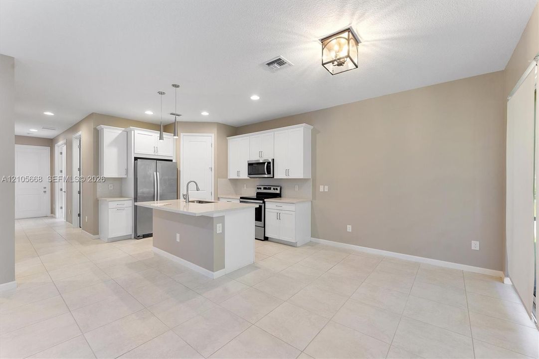 Kitchen featuring white cabinetry, center island with stone-finish countertop, stainless steel appliances, neutral tile flooring, and metallic pendant lighting