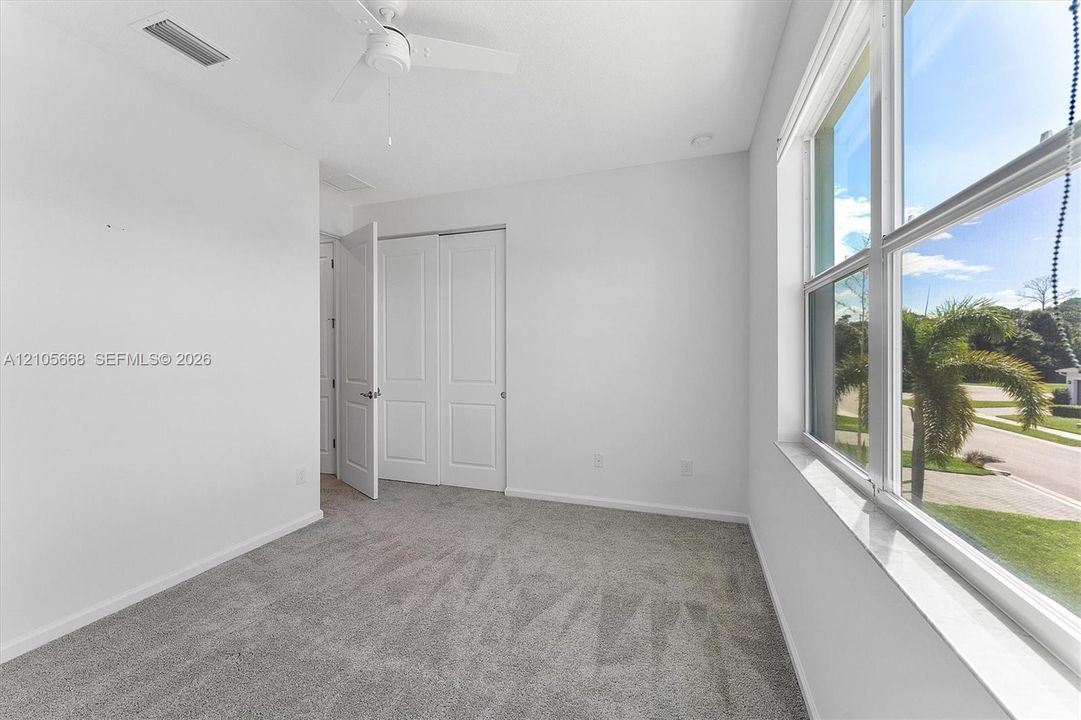 Neutral-toned carpeting, large windows, white paneled closet doors, and a ceiling-mounted fan