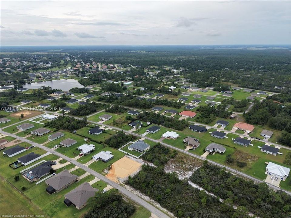 Aerial perspective of a residential development featuring paved street infrastructure, landscaped grass lots, and a water feature