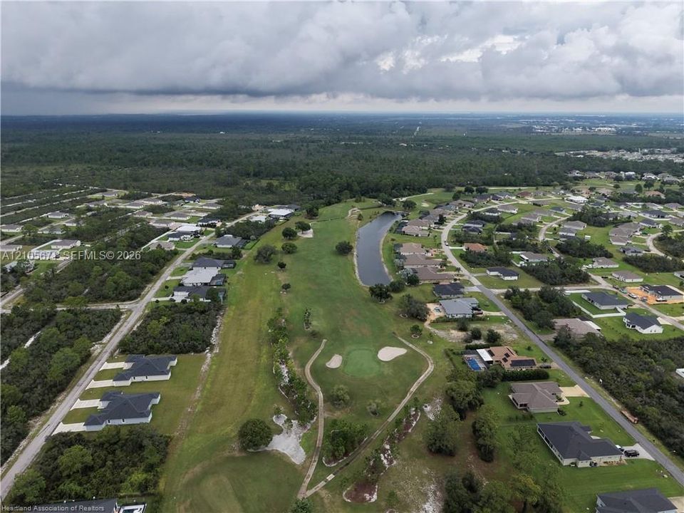 Aerial perspective featuring a golf course, expansive green space, water feature, sand bunkers, and mature trees