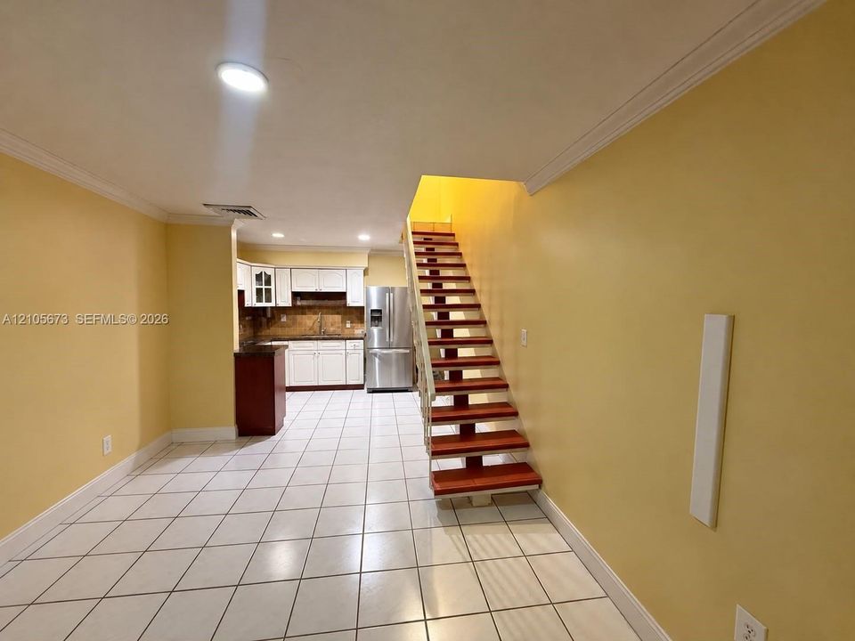 Open-concept interior featuring large-format tile flooring, an open-tread wooden staircase, built-in white cabinetry, and stainless steel kitchen appliances