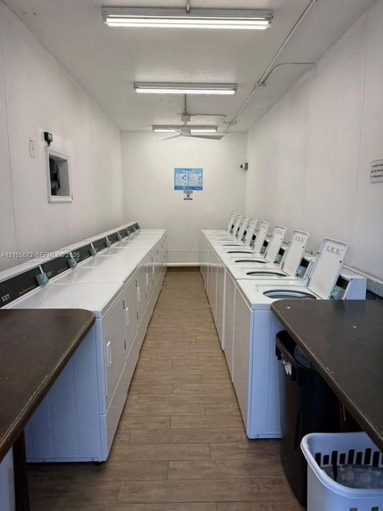 Laundry facility equipped with multiple top-loading washing machines, wood-finish flooring, and built-in folding counters