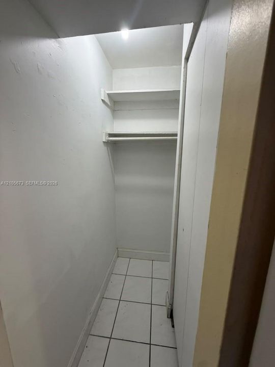 Reach-in closet featuring white ceramic tile flooring, built-in shelving, and a garment rod
