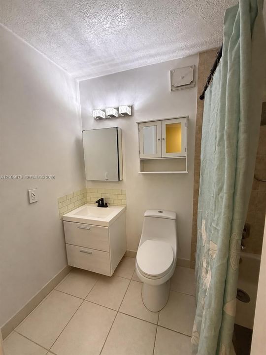 Bathroom featuring a floating vanity with a rectangular sink, wall-mounted three-light fixture, built-in medicine cabinet, and ceramic tile flooring