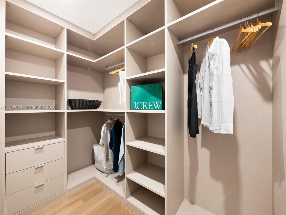 Custom walk-in closet featuring extensive built-in shelving, a dedicated three-drawer dresser unit, integrated hanging rods, and wood-finish flooring. Images are for finish purposes only. Please refer to the floor plan for the layout.