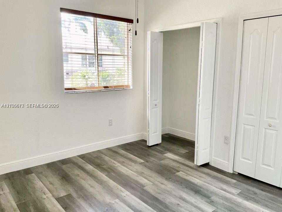Interior space featuring wood-finish flooring, white walls, horizontal window blinds, and dual bi-fold closet doors