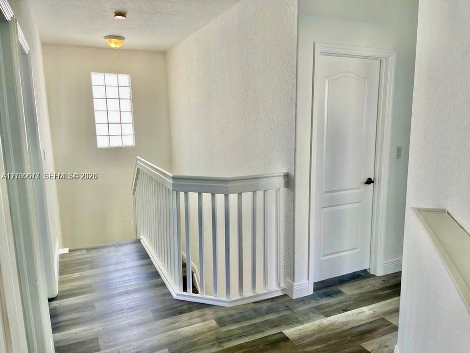 Wood-finish flooring, white spindle railing, glass block window, and dual-panel interior door with matte black hardware