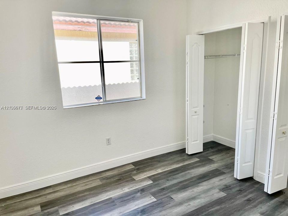 Interior space featuring wood-finish flooring, white walls, a single-pane window, and a built-in closet with multi-panel swinging doors