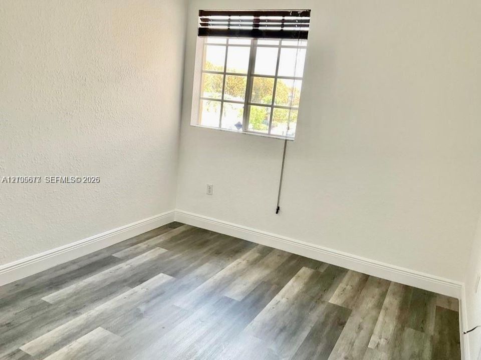 Neutral-toned wood-finish flooring, multi-pane window with horizontal blinds, and textured wall finish