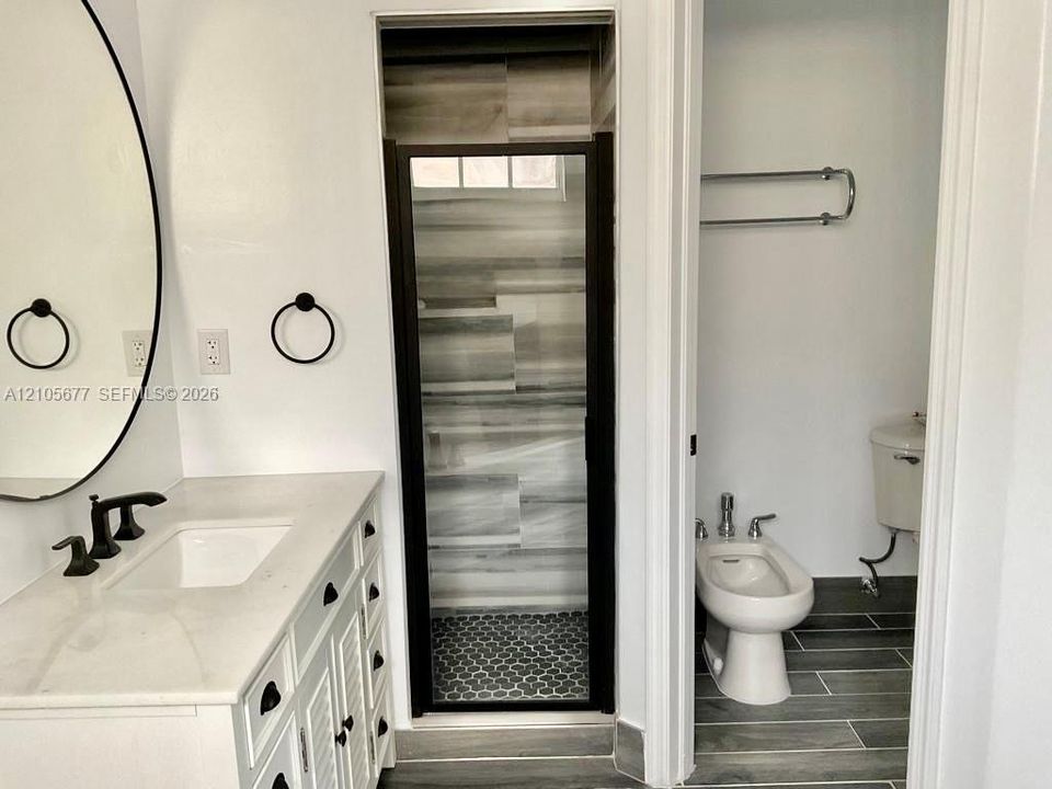 Bathroom featuring a white vanity with a light-toned countertop, undermount sink, matte black widespread faucet, and oval wall-mounted mirror