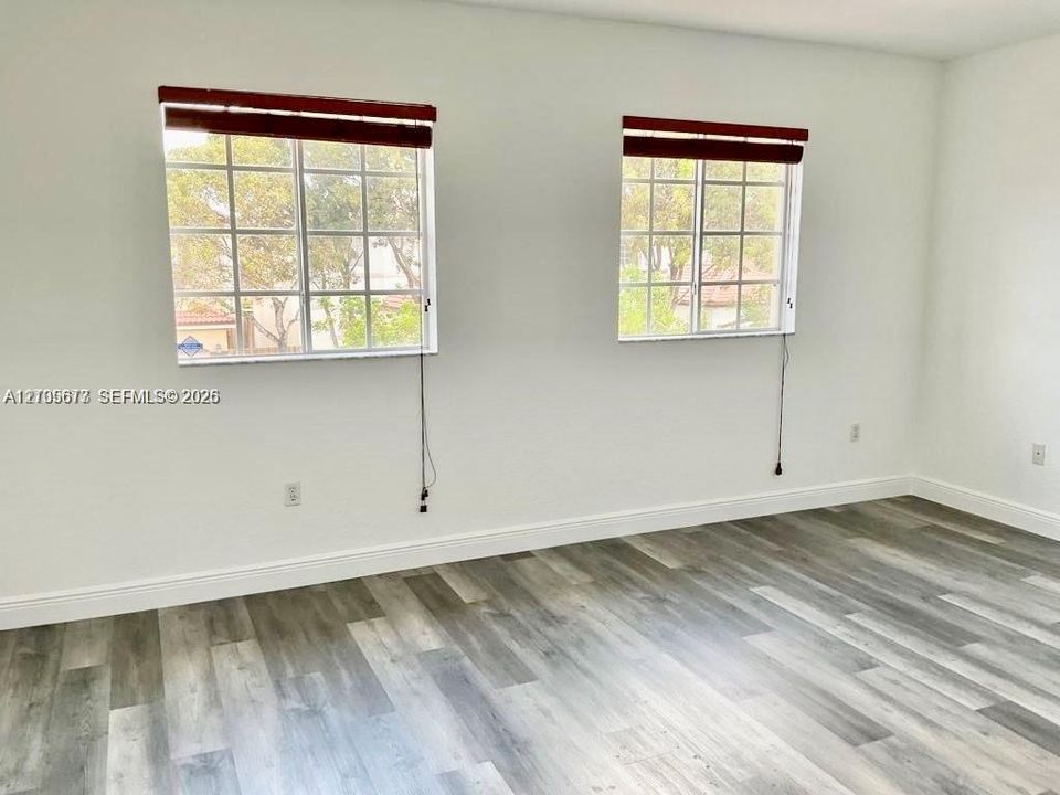 Room featuring wood-finish flooring, dual windows with multi-pane grilles, and horizontal window blinds