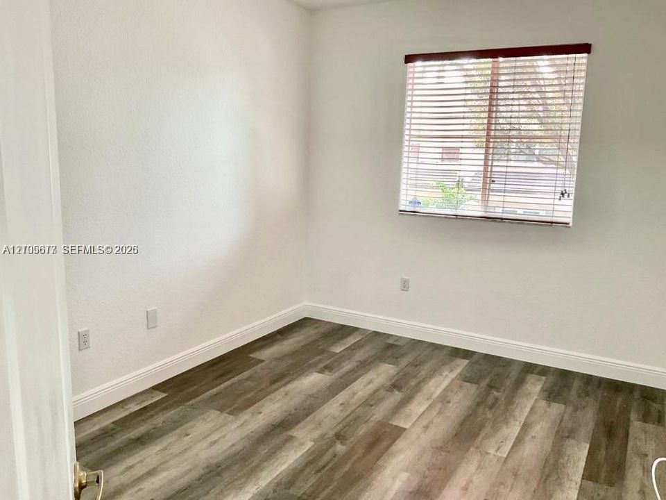 Neutral-toned interior room featuring wood-finish flooring, white walls, and a window with horizontal blinds