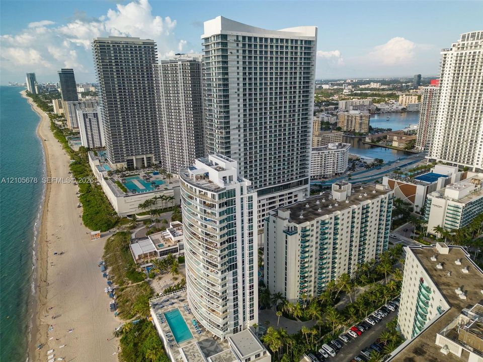 High-rise residential tower featuring floor-to-ceiling windows and private balconies, situated on a coastal shoreline with direct beach access and a ground-level swimming pool