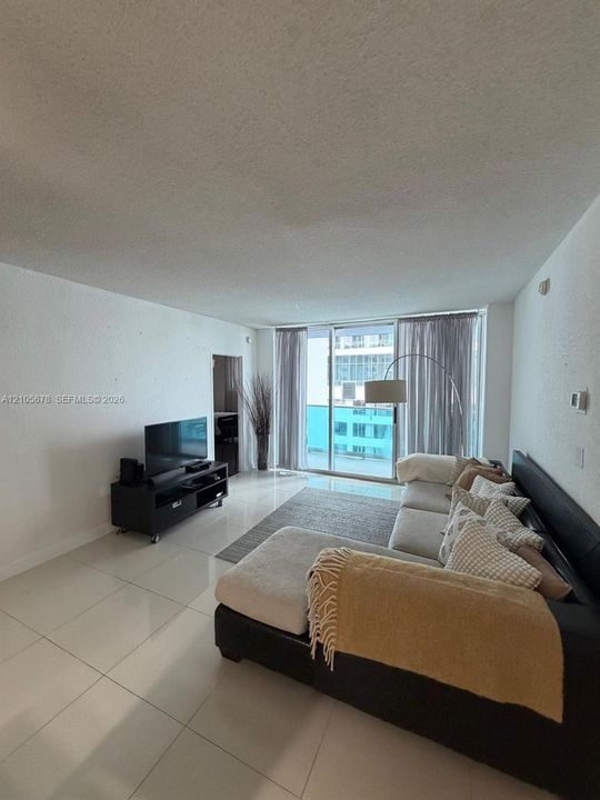 Large format porcelain tile flooring, textured walls, and floor-to-ceiling sliding glass doors opening to a balcony