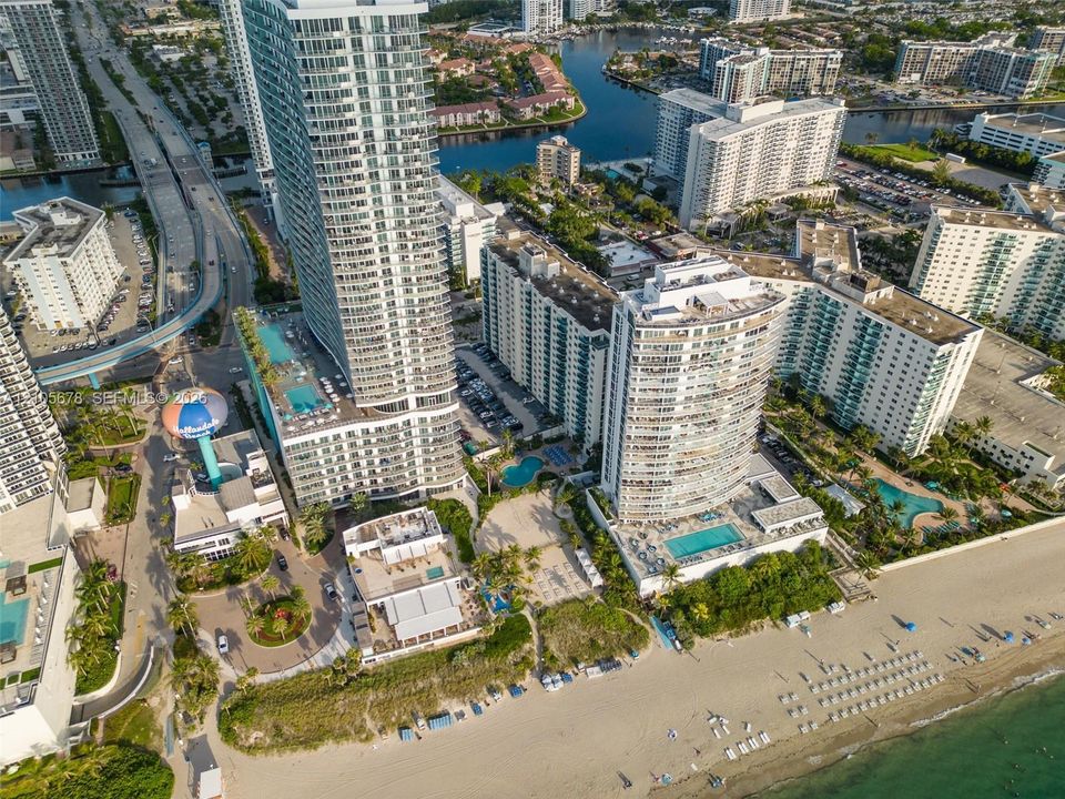 Aerial perspective of high-rise structures featuring integrated outdoor swimming pools, multi-level parking facilities, and direct shoreline access