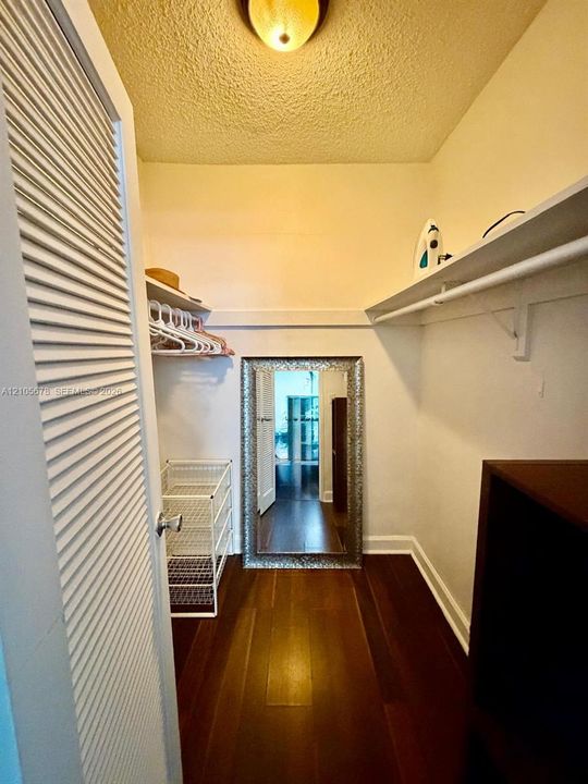 Storage space featuring louvered bi-fold doors, wood-finish flooring, and built-in upper shelving with integrated hanging rods