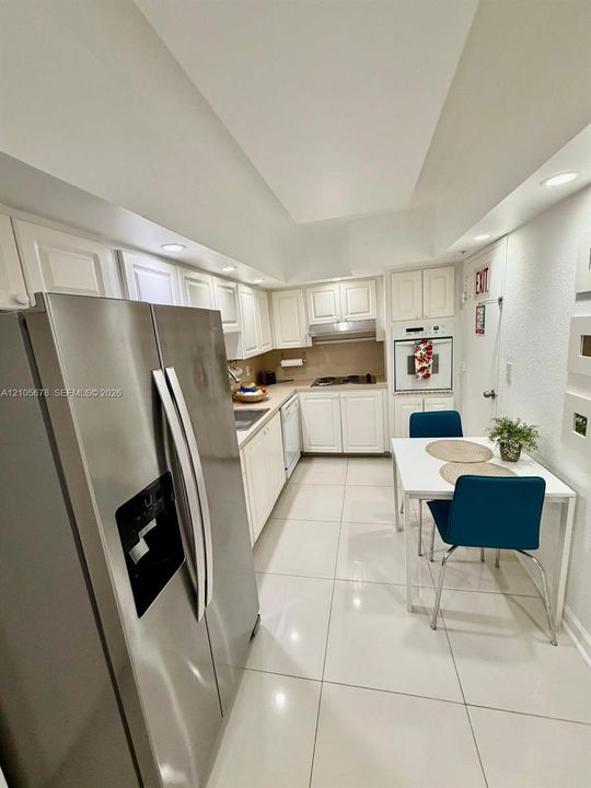 Kitchen featuring white cabinetry, stainless steel side-by-side refrigerator, built-in wall oven, recessed lighting, and large-format tile flooring