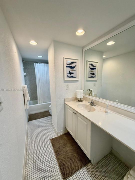 Vanity featuring white cabinetry, a solid surface countertop with an integrated basin, a polished chrome faucet, and a large wall-mounted mirror with a white frame, accompanied by recessed lighting and tiled flooring