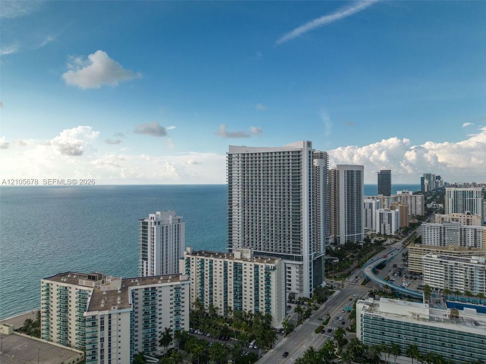 Aerial perspective of coastal high-rise architecture featuring glass-railed private balconies, prominent oceanfront positioning, and proximity to expansive shoreline