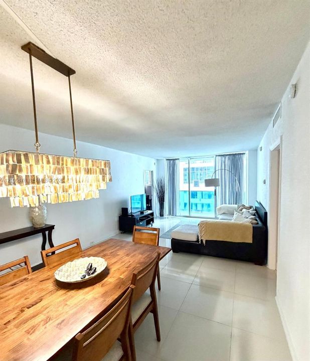 Rectangular light fixture with metallic pendant detailing, large-format tile flooring, and floor-to-ceiling glass sliding doors leading to an exterior balcony