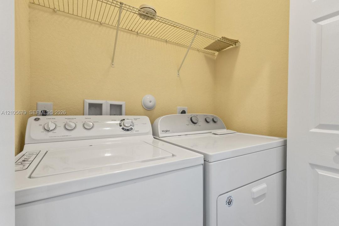 Utility space featuring white top-load washer and dryer units, integrated wall-mounted wire shelving, and recessed electrical and water hookups