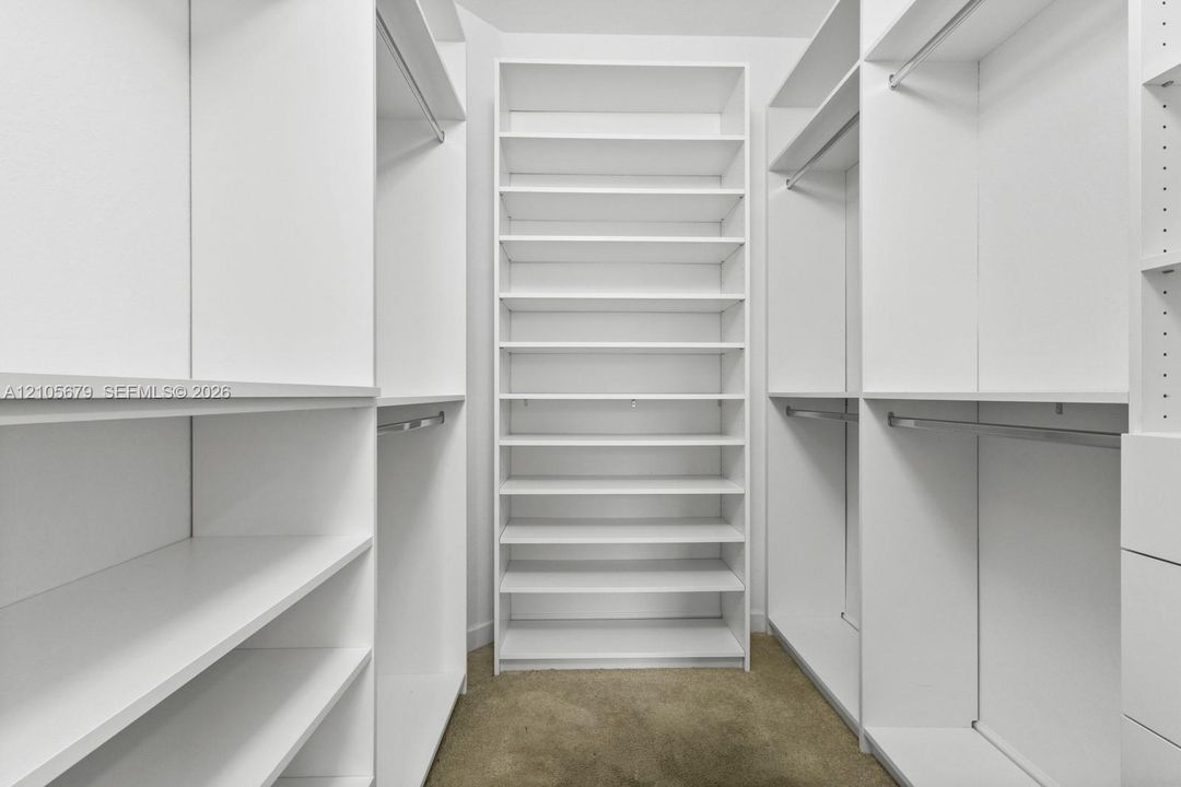 Walk-in closet featuring white built-in shelving, multiple adjustable storage cubbies, and integrated metal clothing rods