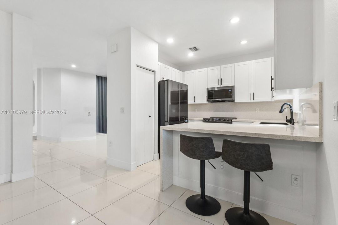 Kitchen featuring white shaker-style cabinetry, a stone-surface breakfast bar, recessed lighting, and tile flooring