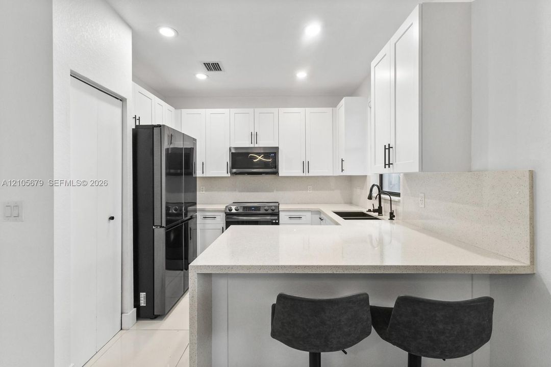 Kitchen featuring white Shaker-style cabinetry, quartz countertops, a stone-surfaced backsplash, black hardware, and recessed lighting