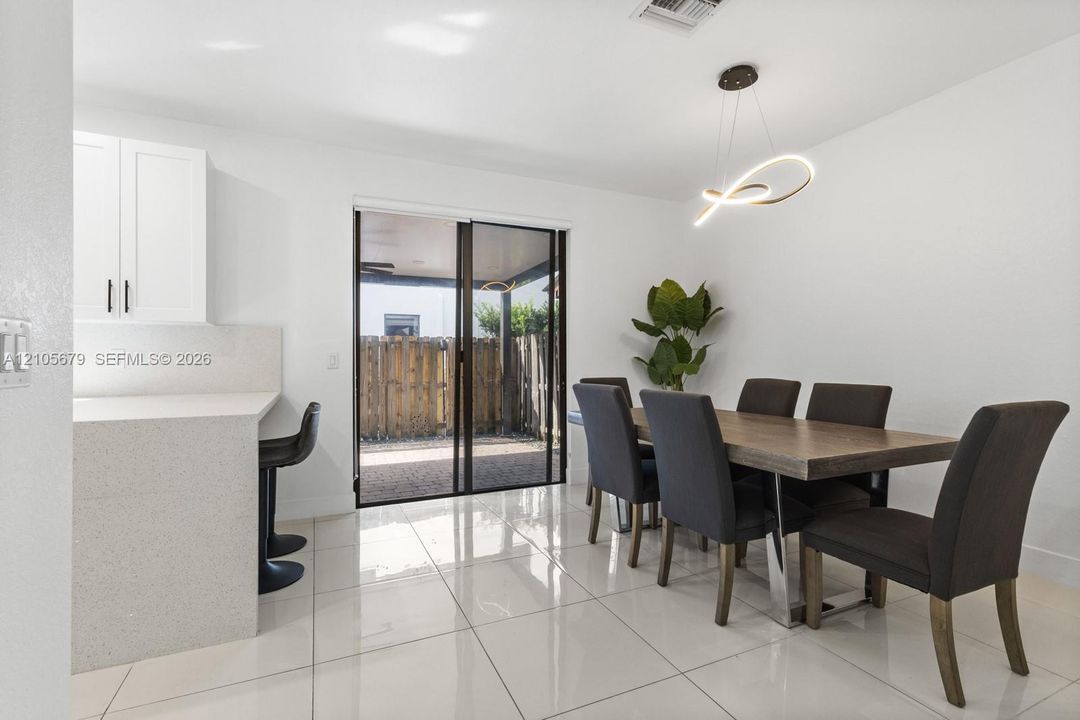 Polished porcelain flooring, quartz breakfast bar, white cabinetry, architectural LED pendant lighting, and sliding glass patio doors