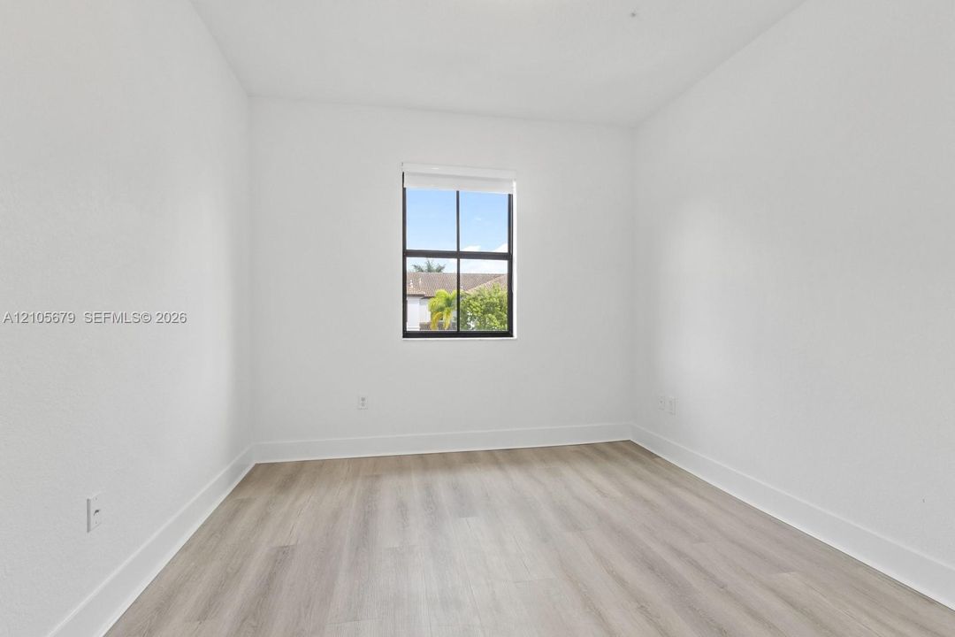 Neutral interior room featuring wood-finish flooring, crisp white walls, and a single window with black grid framing