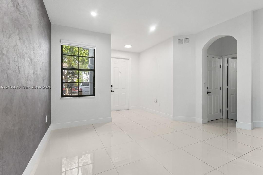 Interior space featuring a textured gray accent wall, large-format tile flooring, recessed lighting, a grid-pane window, and a prominent arched entryway