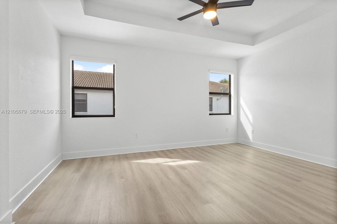 Room featuring tray ceilings, wood-finish flooring, dual windows with dark frames, and a central ceiling fan with integrated lighting
