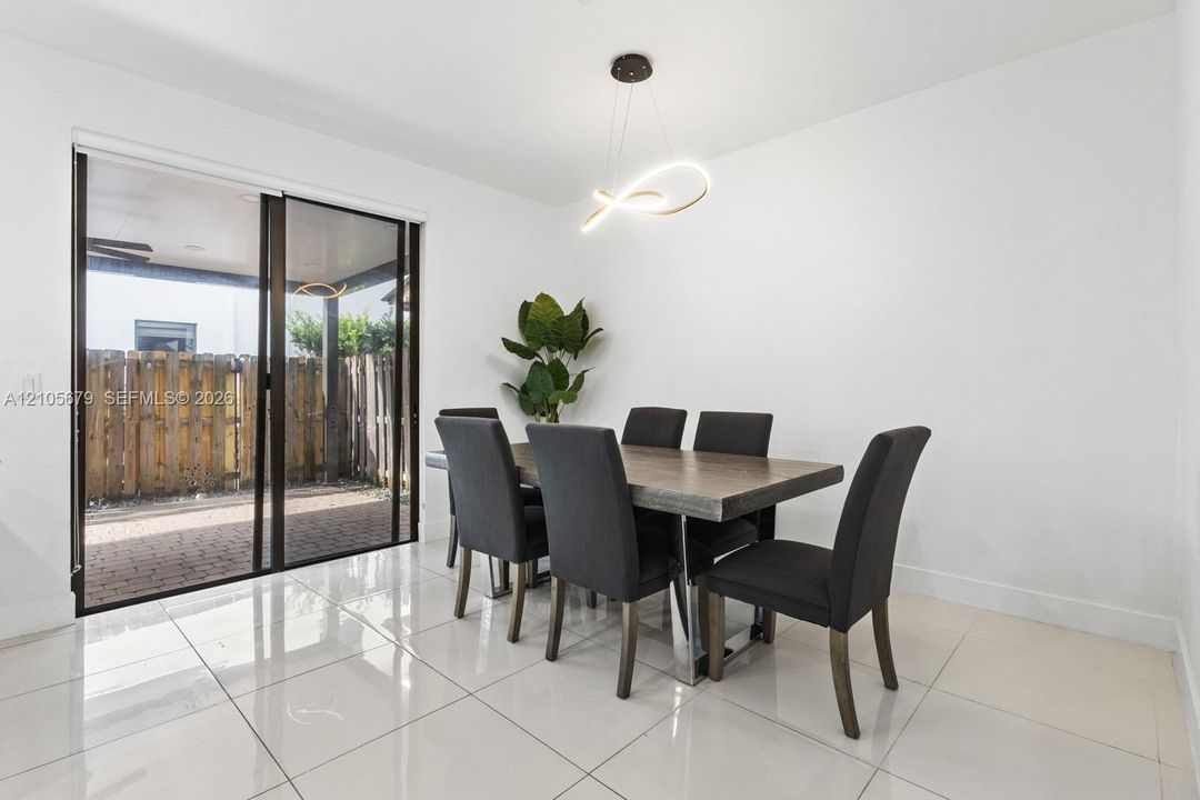 Large-format neutral tile flooring, modern sculptural pendant lighting, and oversized sliding glass doors leading to a paved patio area
