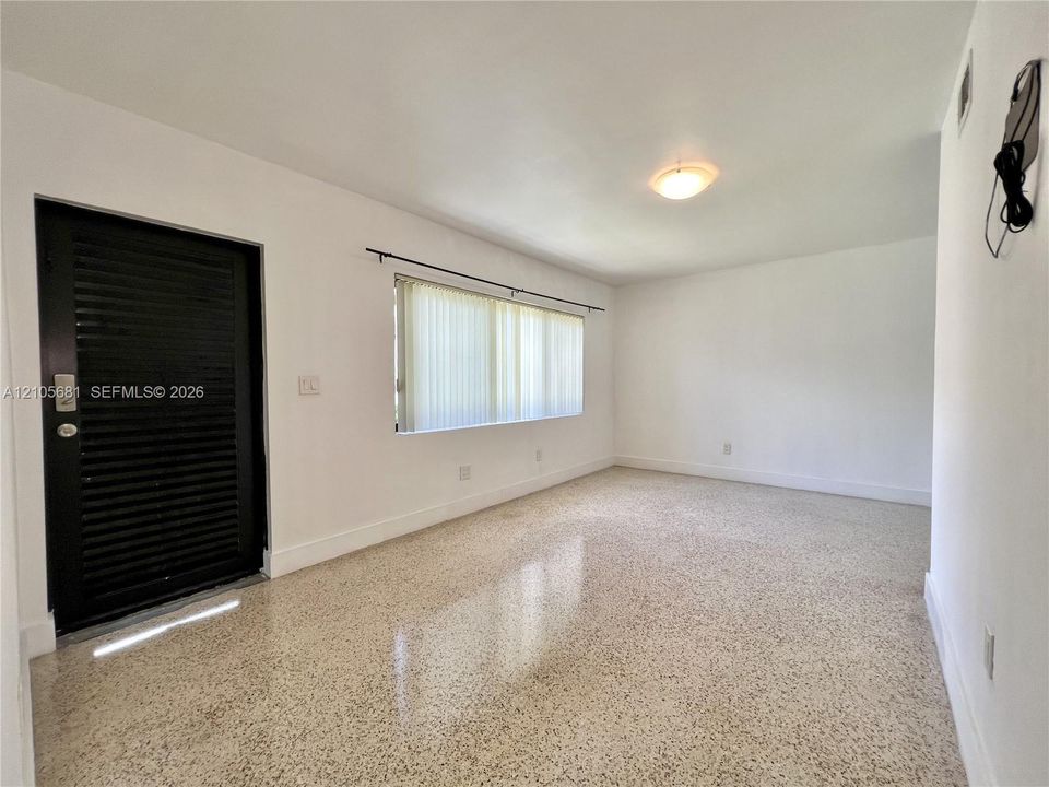 Interior space featuring polished terrazzo flooring, neutral wall finishes, a black entry door, and a horizontal window with mounted hardware